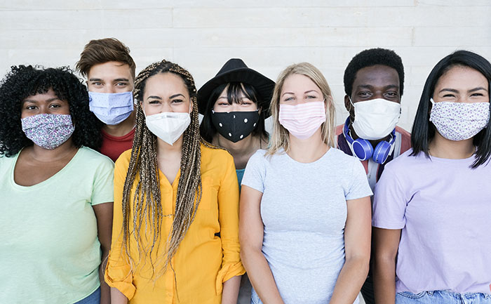 Happy multiracial friends laughing and wearing protective face mask - Group of young peoples having fun together - Concept of lifestyle, health care and the new normality